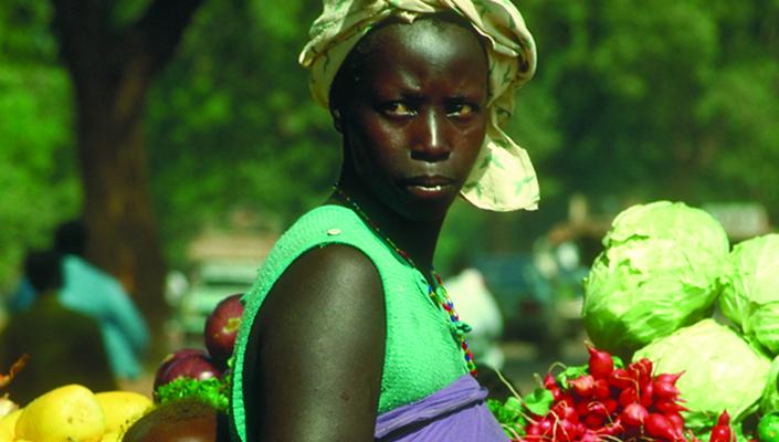 An African woman in a produce market carries her baby in a wrap on her back