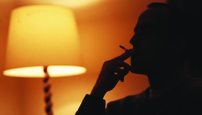 silhouette of a person smoking in the light of a living room lamp