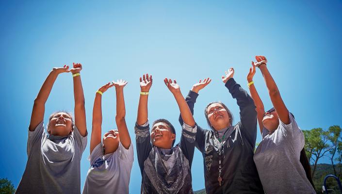 A group of teens raise their hands to the sky in celebration.