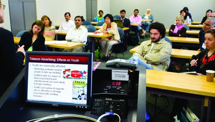 Students in a classroom listen to a talk on Tobacco Advertising: Effects on Youth, which is visible on the presenter's laptop monitor