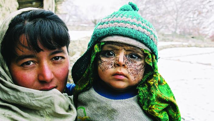 A mother holding her son, who wears a knit cap and a paste on his face as protection from the cold