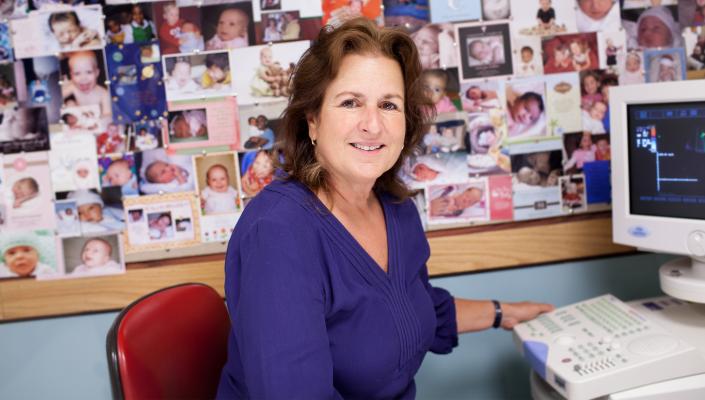 Janet DiPietro with a corkboard filled with baby pictures behind her