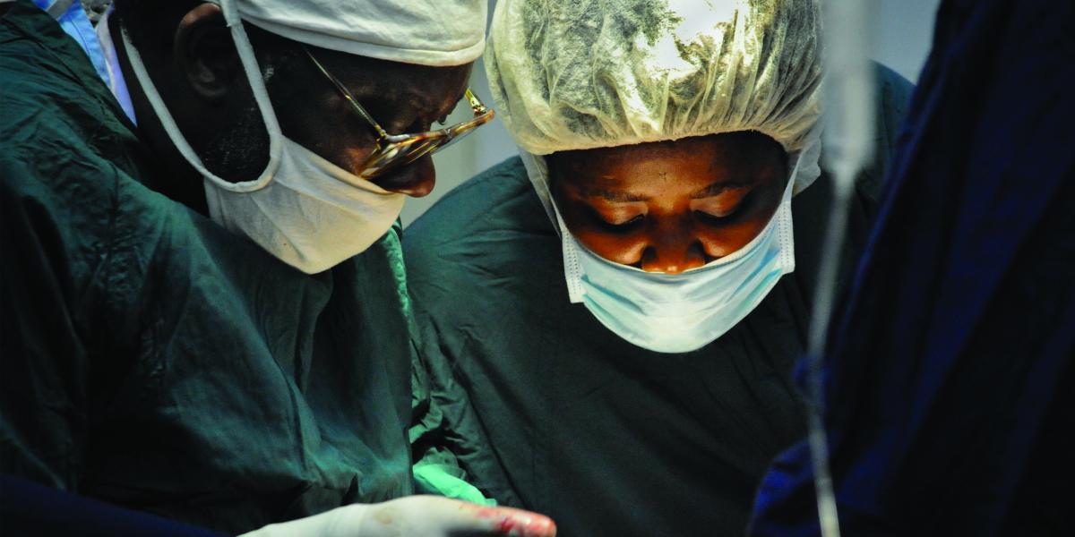 Dr. James Boima and a surgical nurse, both in surgical masks and caps, during a procedure