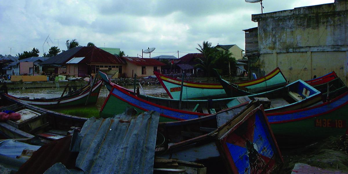 boats and debris such as corrugated metal are tossed on land next to a brick concrete building
