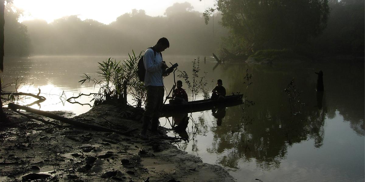a researcher uses a G.I.S. device at the edge of the Amazon, where two children sit