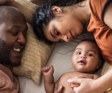 Parents lay with their infant on a bed.