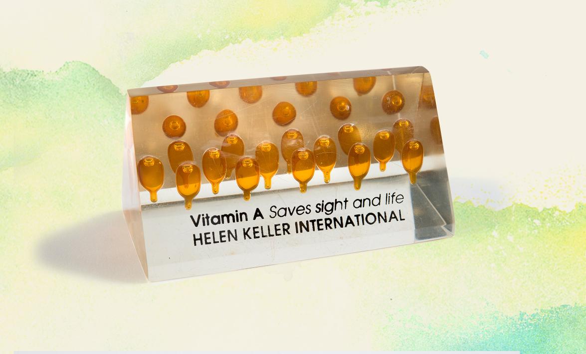 a paperweight with vitamin A capsules inside and a label that says "Vitamin A saves sight and life, Hellen Keller International"
